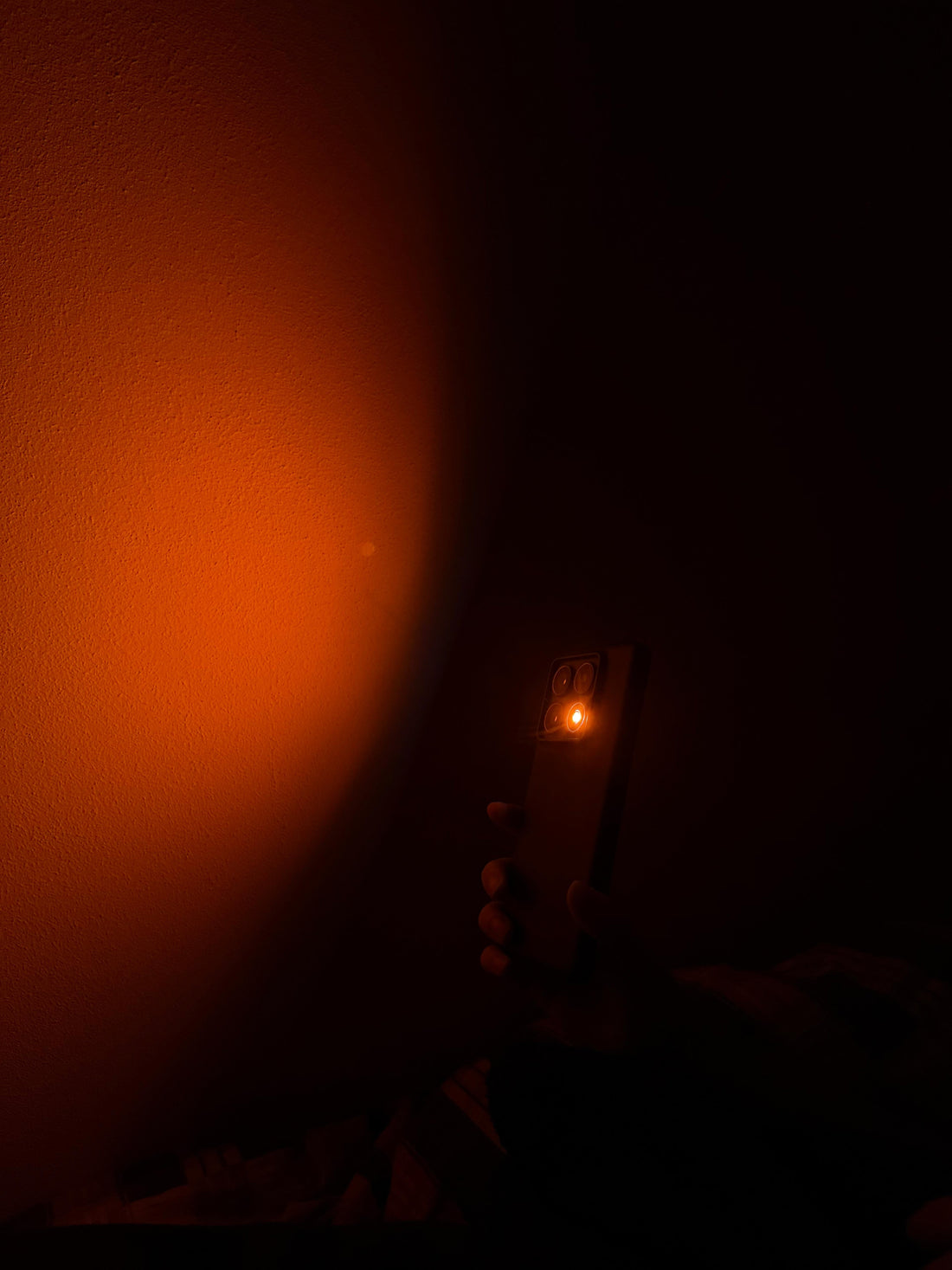 Power outage ideas: a hand holding a phone that casts warm orange light onto the wall