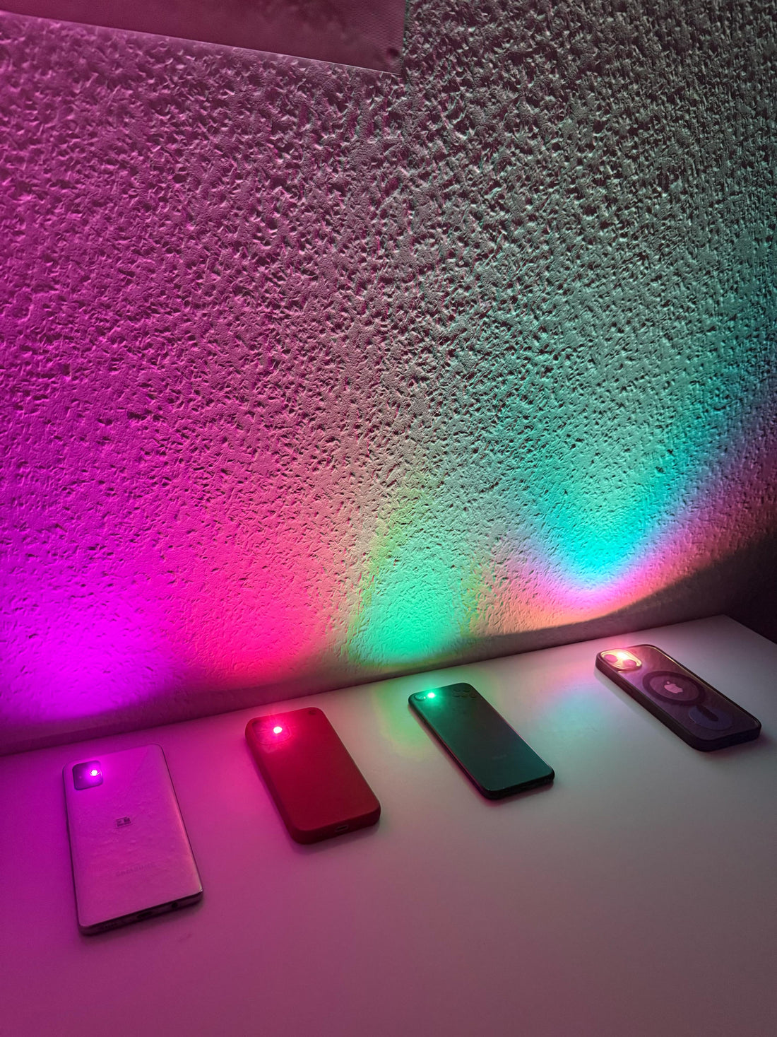 DIY disco lights: four phones on a shelf casting violet, pink, green and turquoise light onto the wall