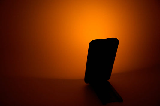 Getting dark early: a phone on a stand casting orange light onto the wall