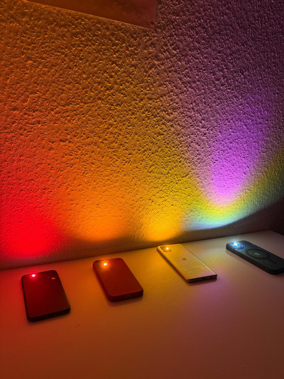 Discoteca in casa: quattro telefoni su una mensola proiettano luce rossa, arancione, gialla e viola sulla parete