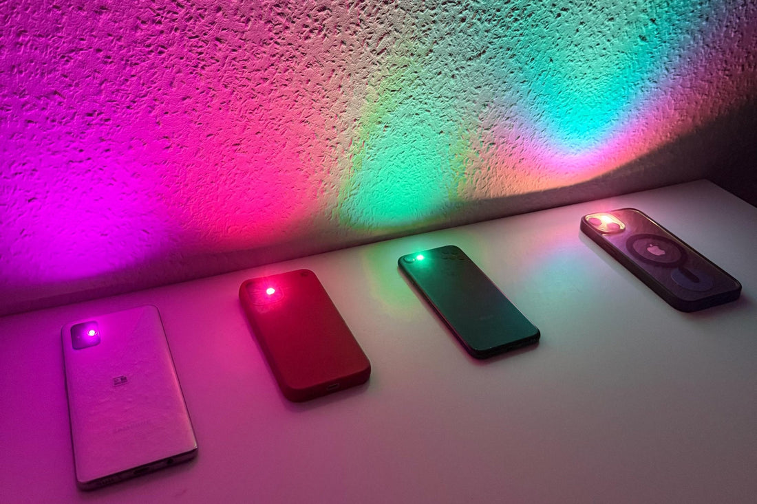 Four phones with FlashyHue color filters casting pink, red, green and turquoise light on a white wall