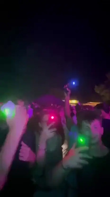 Crowd partying at night with green, pink and blue phone lights