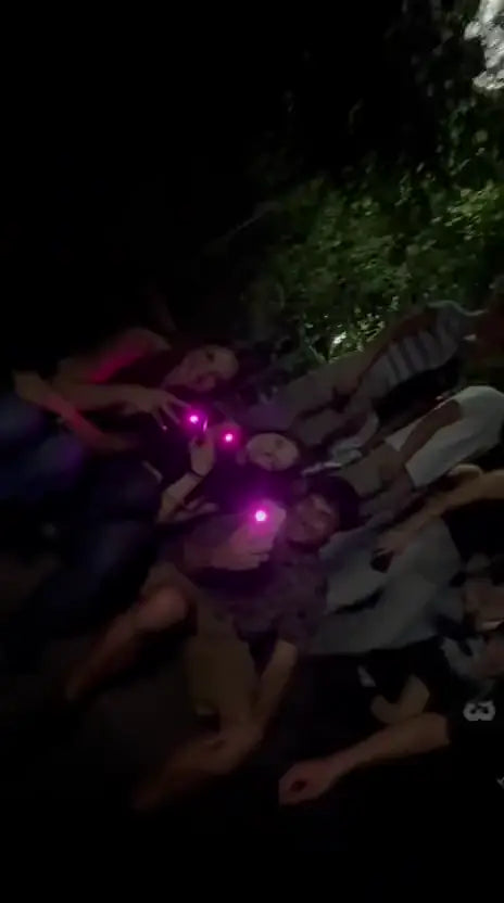 Group lying in the grass at night holding up phones with pink light