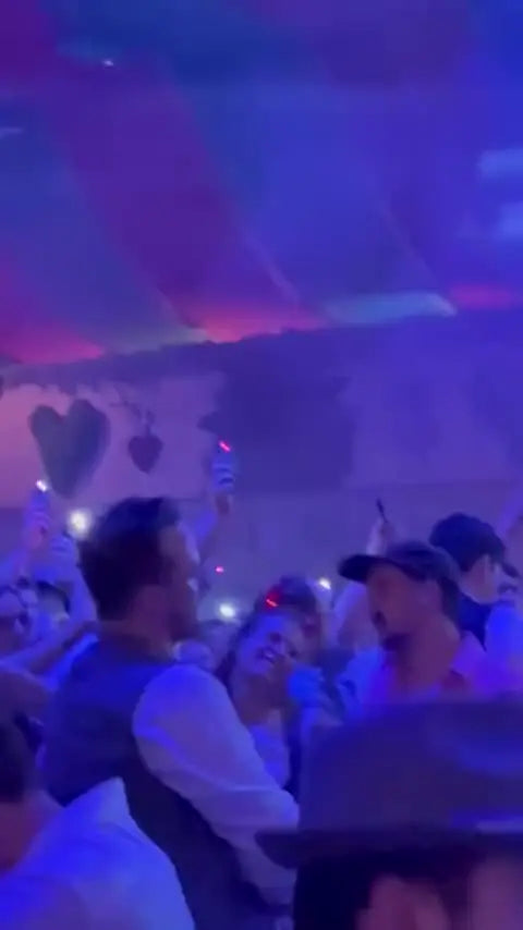 Partygoers in a festival tent holding up phones with green, red and pink light
