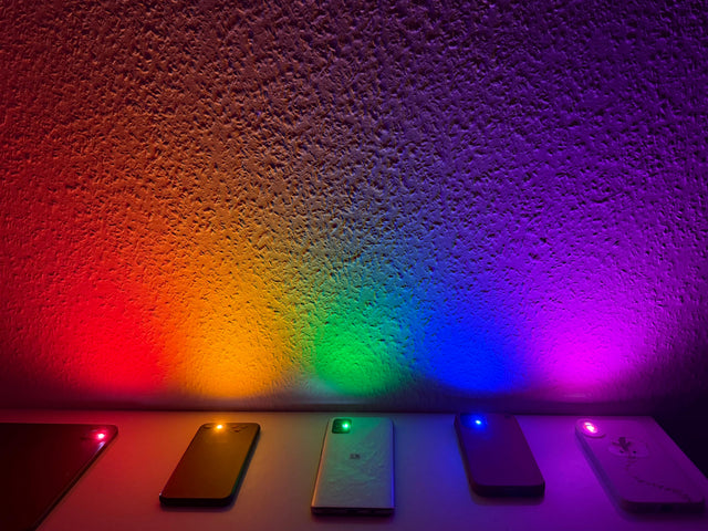 Rainbow-coloured light from several phones on a wall